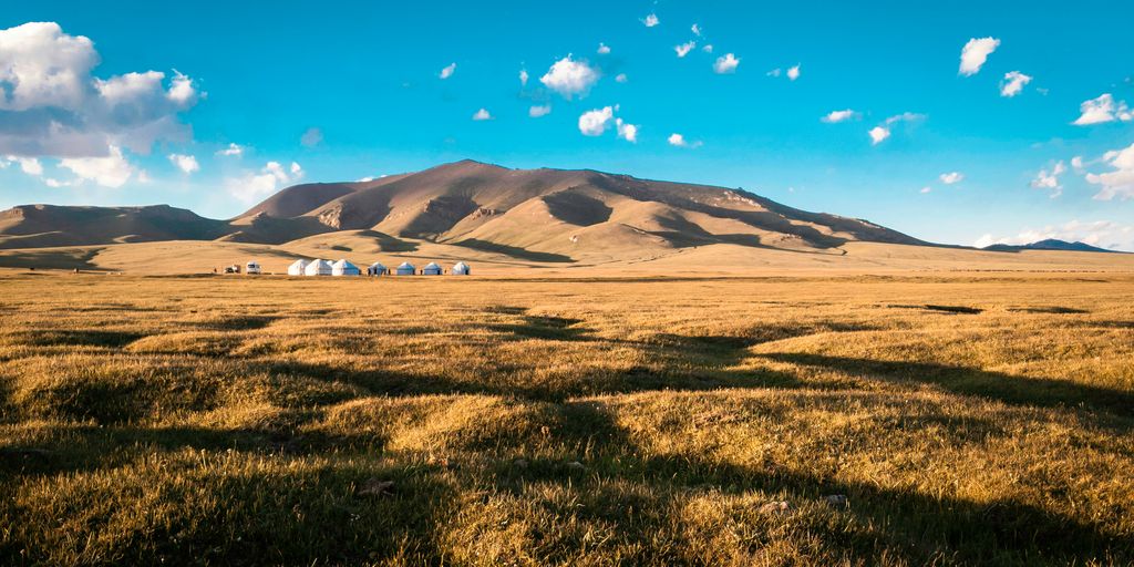 green grass field near mountain under blue sky during daytime